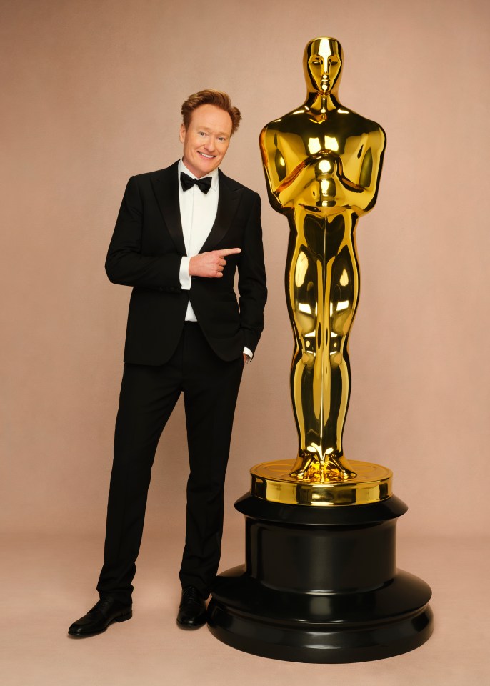 Conan O'Brien in a tuxedo pointing at an Oscar statuette.