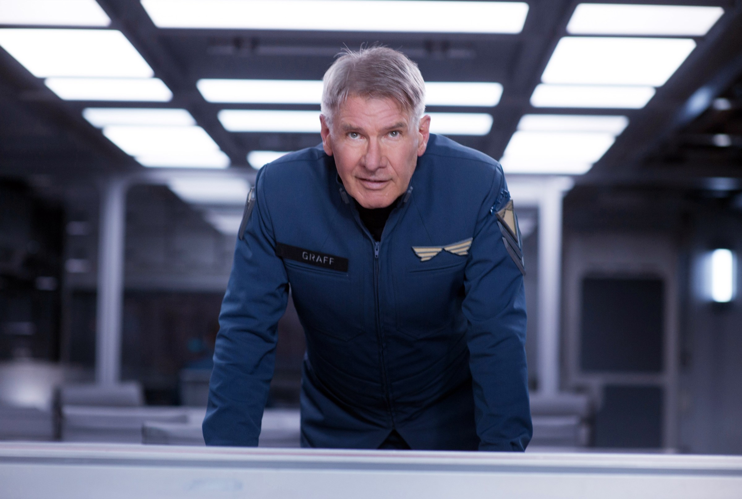 Harrison Ford in a futuristic space uniform leaning over a table in Ender’s Game