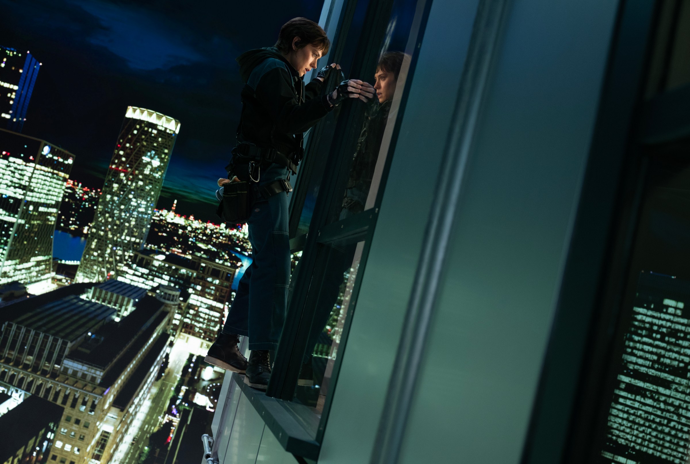 In Cleaner, Daisy Ridley stands on a window ledge up very high on an office building