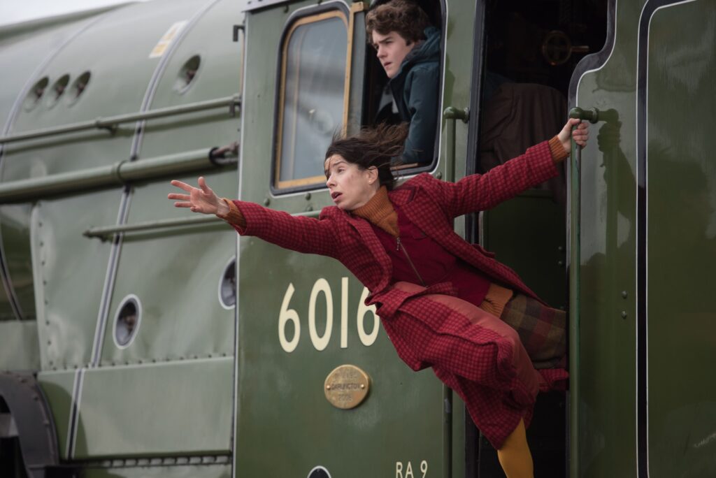 Sally Hawkins wearing all red and leaning out of a moving train, one hand extended, in Paddington 2