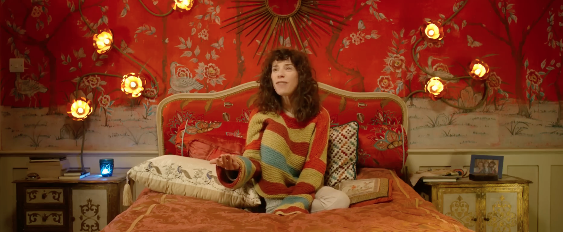 Sally Hawkins sitting on her bed, knee tucked into her big striped sweater in Paddington