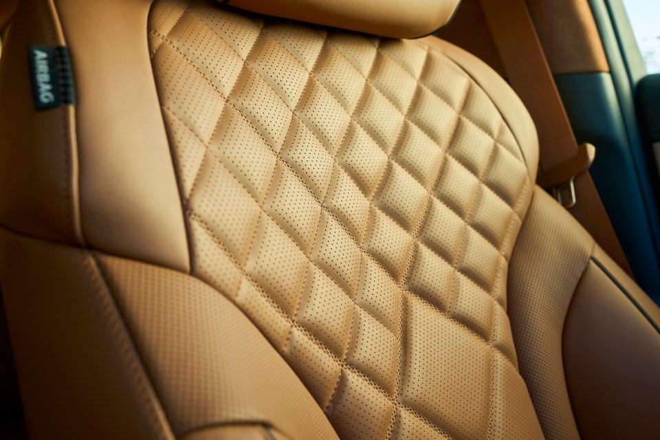 Close-up of tan leather car seat with diamond stitching and perforated pattern.