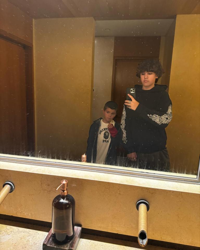 Mirror reflection of two boys taking a selfie in a bathroom.