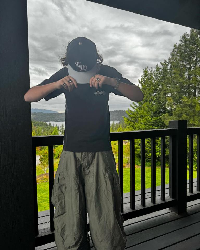 Person holding a hat in front of their face on a deck overlooking a lake and trees.