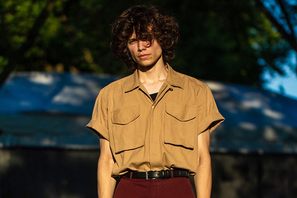 Portrait of a young man wearing a tan shirt and maroon pants.