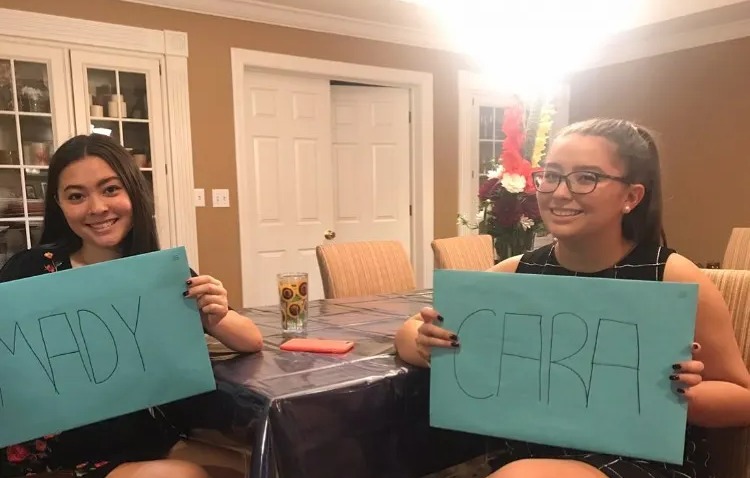 Two women holding signs with their names, Maddy and Cara.