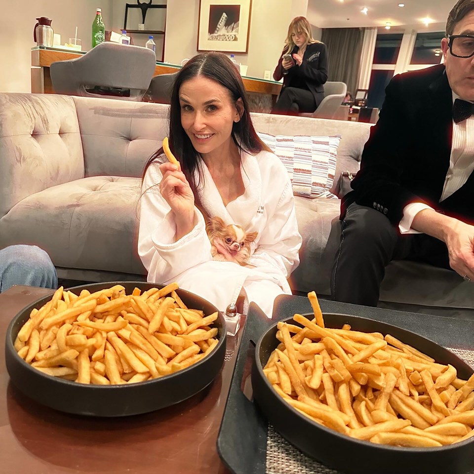 Woman in bathrobe with small dog eating french fries.