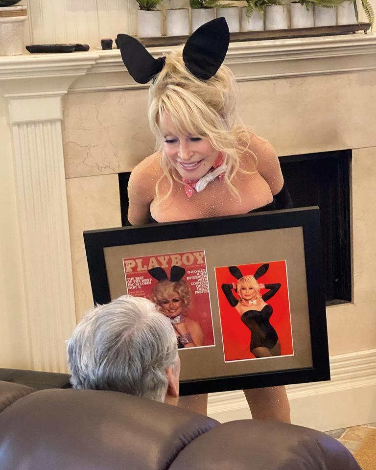 Dolly Parton in a Playboy Bunny costume showing her husband a framed Playboy magazine featuring her.