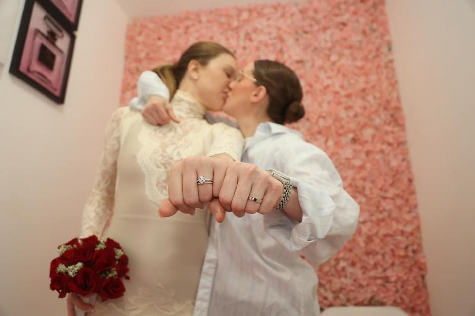 A bride and groom kissing, showing off their wedding rings.