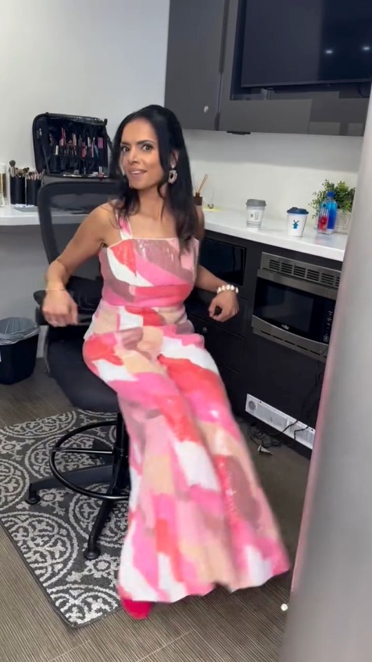 Woman in pink and white patterned jumpsuit sitting in office chair.