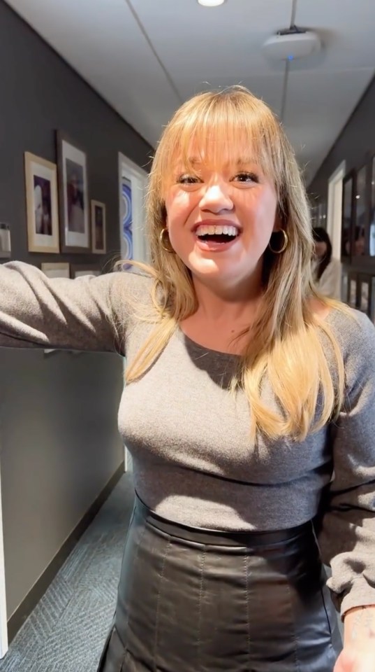 Kelly Clarkson smiling in a hallway.