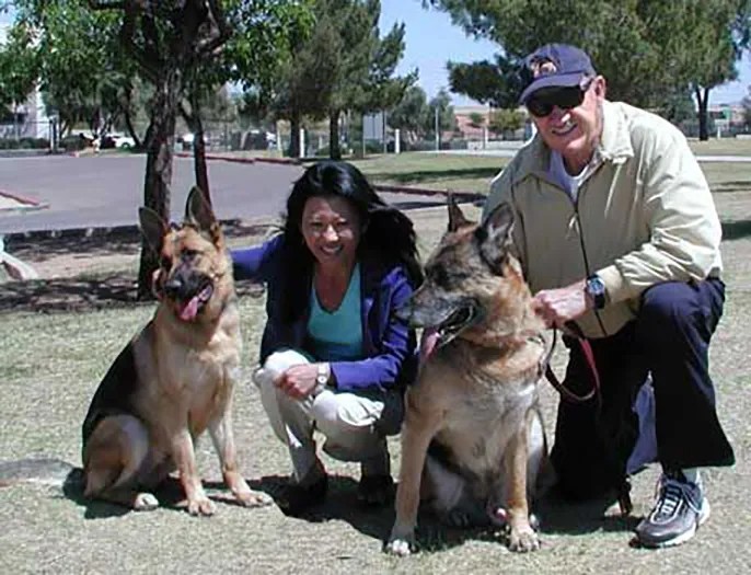 Couple with two German Shepherds in a park.