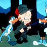 A cartoon rabbit dressed as a duck and a duck dressed a rabbit flank a hunter in green and red clothing holding a shotgun.