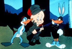 A cartoon rabbit dressed as a duck and a duck dressed a rabbit flank a hunter in green and red clothing holding a shotgun.