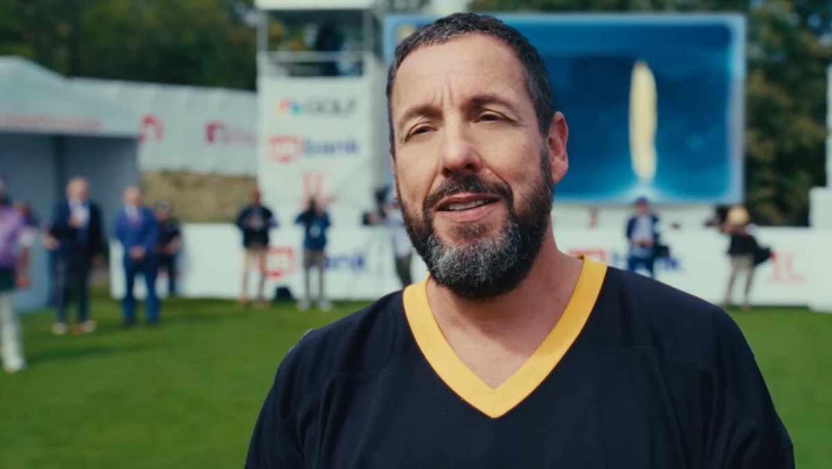 Adam Sandler com uma barba começando a sorrir no campo de golfe em Happy Gilmore 2