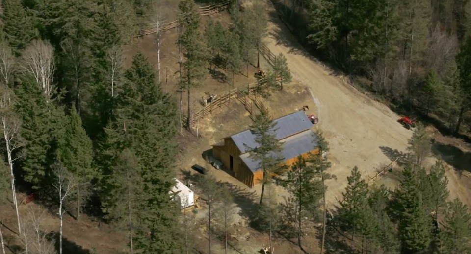 Aerial view of a wooden barn and surrounding property in a wooded area.