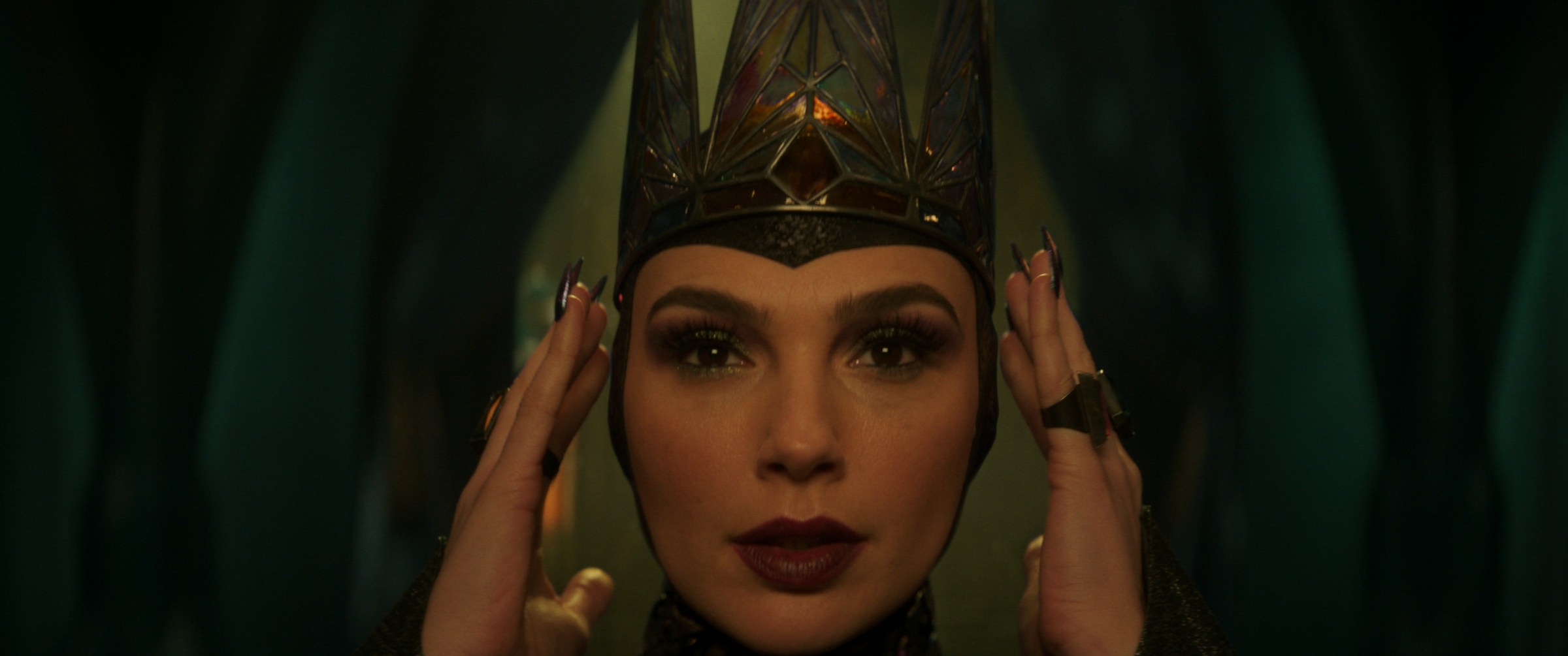 Gal Gadot as the Evil Queen, adjusting her crown. From Snow White.