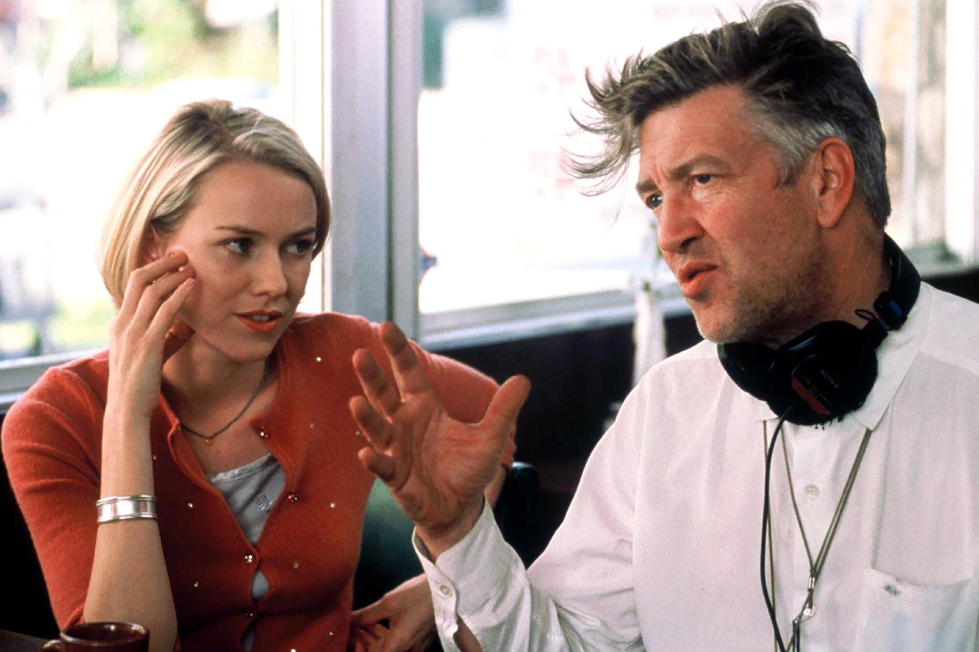 A woman takes notes from a director in a diner booth.