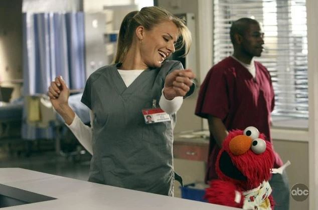 A nurse dances with Elmo in a hospital.