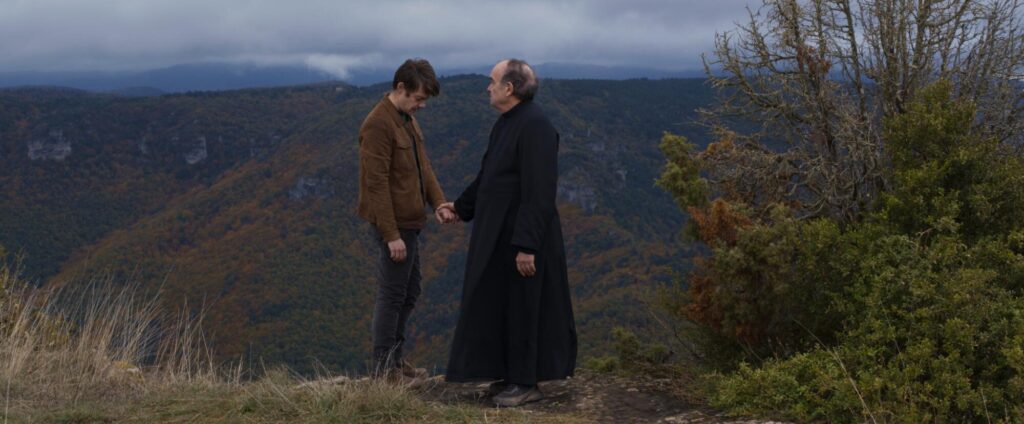 A priest and a man hold hands in a windy field.