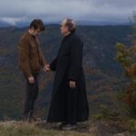 A priest and a man hold hands in a windy field.