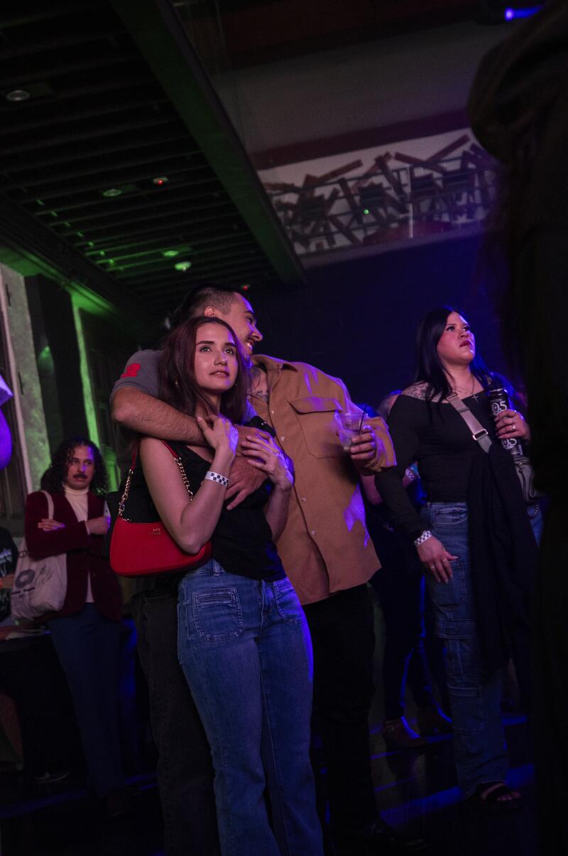 People stand watching a concert, including a couple, he with his arm around her