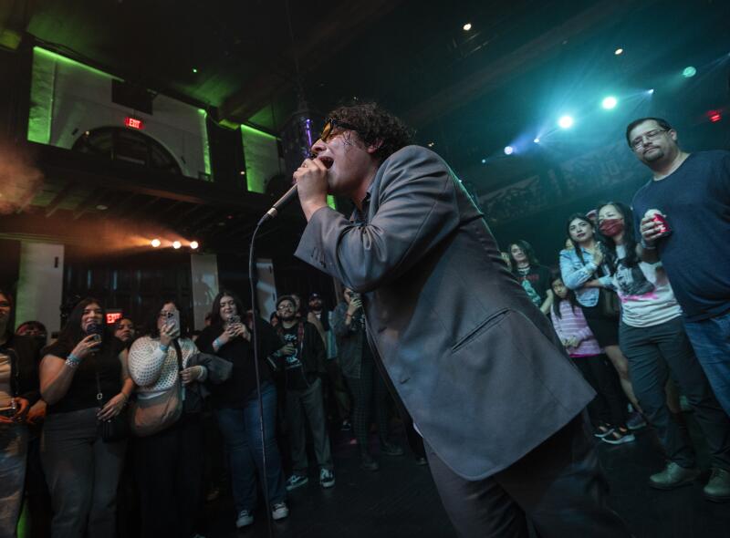 People stand in a semicircle around a person singing intensely into a microphone.