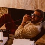 Ben Affleck on the phone, wearing glasses and a cable knit sweater.