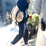 Man walking down a city street, carrying a tote bag and a coffee cup.