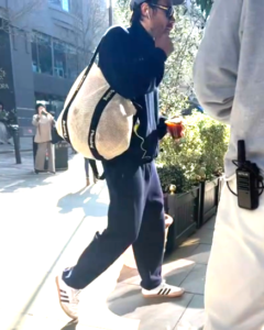 Man walking down a city street, carrying a tote bag and a coffee cup.