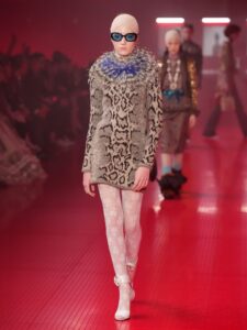 Model in a patterned sweater and white lace tights walking a runway.