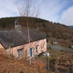 Pink cottage with a small wind turbine on the roof, nestled in a valley.