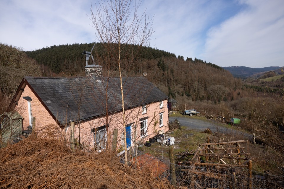 Pink cottage with a small wind turbine on the roof, nestled in a valley.