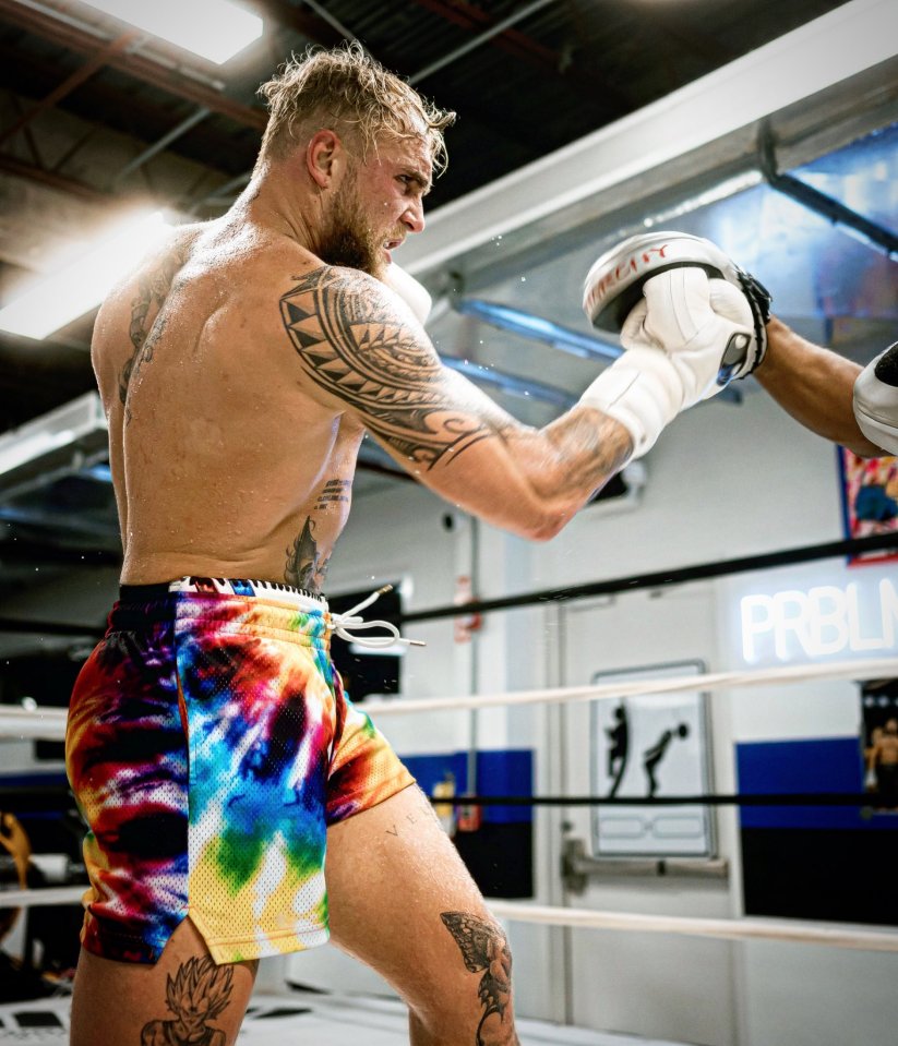 A tattooed boxer throwing a punch in a boxing ring.