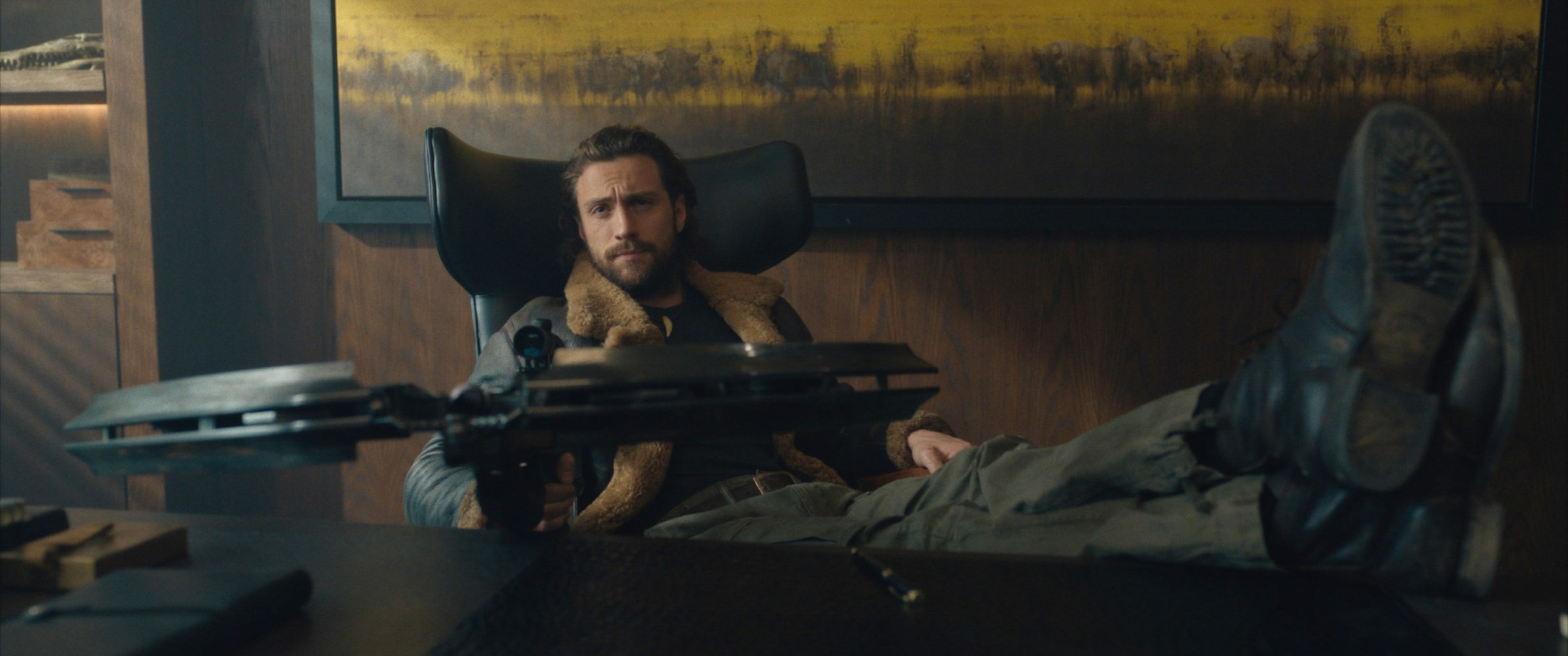 Aaron Taylor-Johnson as Kraven, sitting with his feet up behind a fancy office desk, casually aiming a massive crossbow.