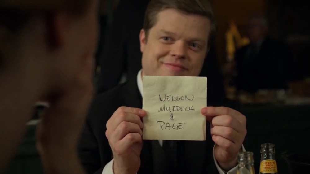 Foggy Nelson holds up a cocktail napkin with the words “Nelson, Murdock & Page” written on it in Daredevil season 3.