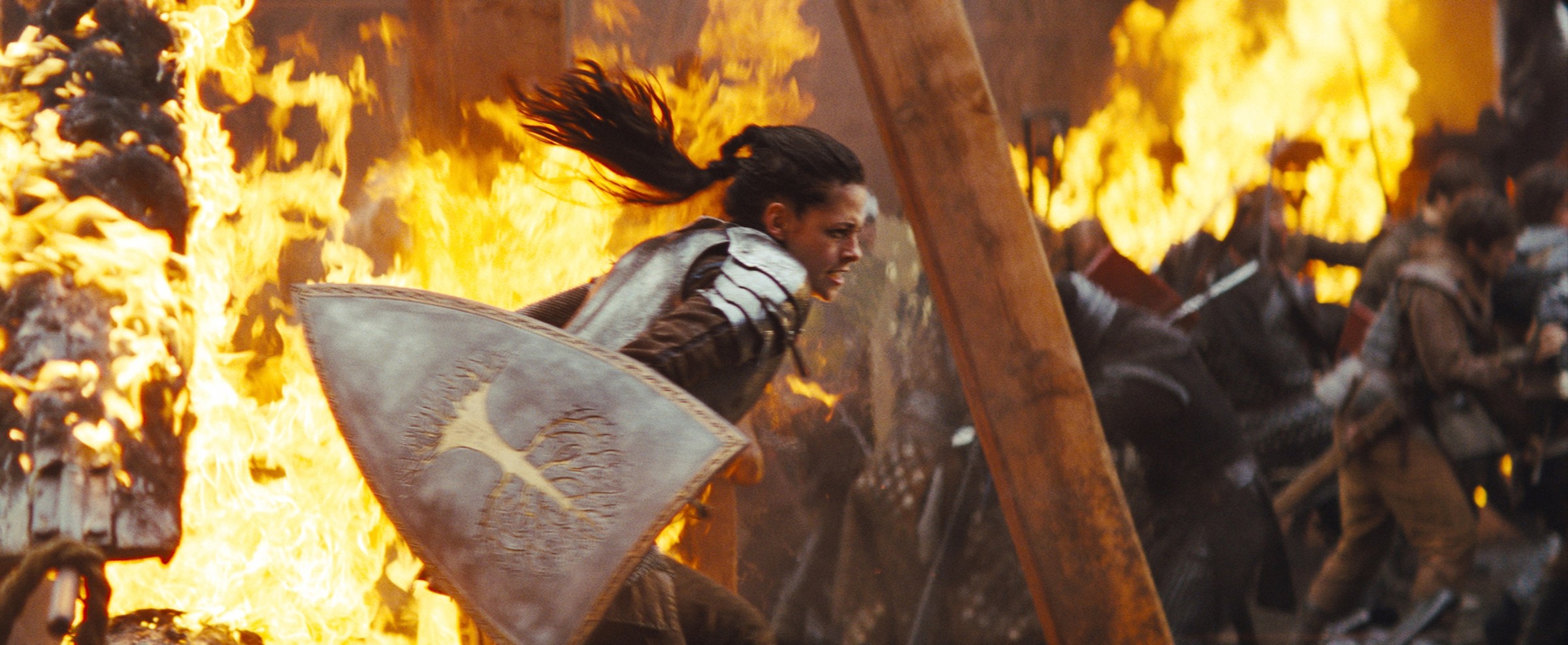 Snow White clad in armor with a shield, charging into a fight, as the battlefield erupts in flames around her. From Snow White and the Huntsman