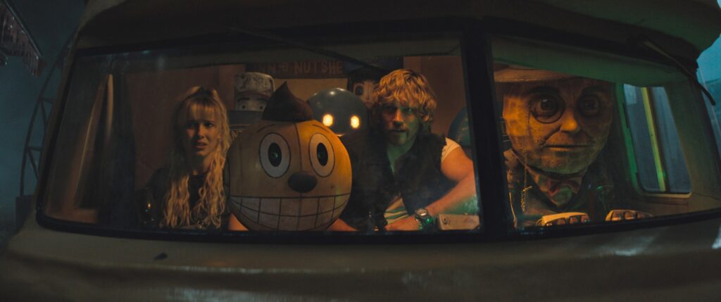 Michelle (Millie Bobbie Brown), Cosmo (a robot with a huge, grinning, round yellow head), Keats (Chris Pratt), and Mr. Peanut (who looks like Mr. Peanut) ride in a van in The Electric State