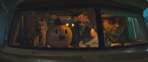 Michelle (Millie Bobbie Brown), Cosmo (a robot with a huge, grinning, round yellow head), Keats (Chris Pratt), and Mr. Peanut (who looks like Mr. Peanut) ride in a van in The Electric State