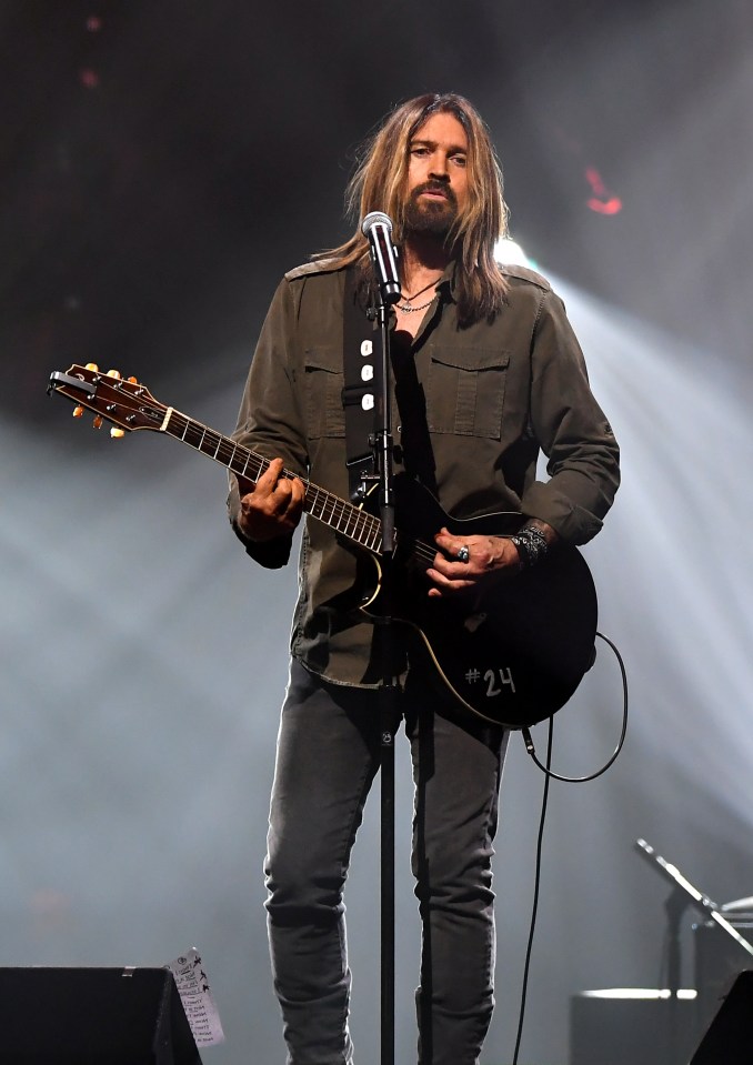 Billy Ray Cyrus performing onstage with a guitar.