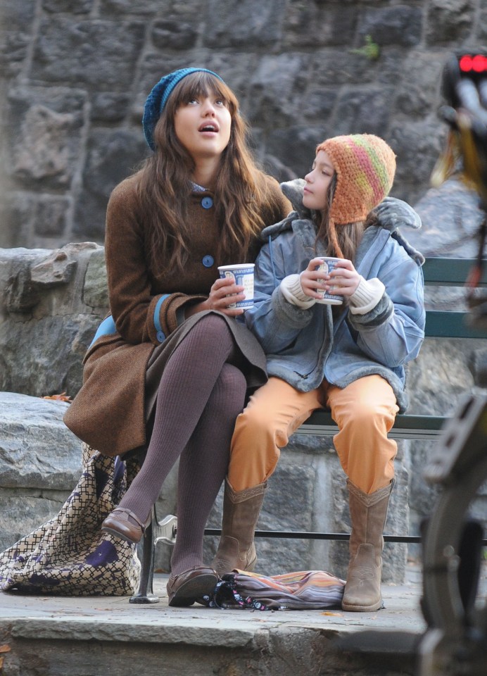 Jessica Alba and a young girl on a park bench, holding coffee cups.
