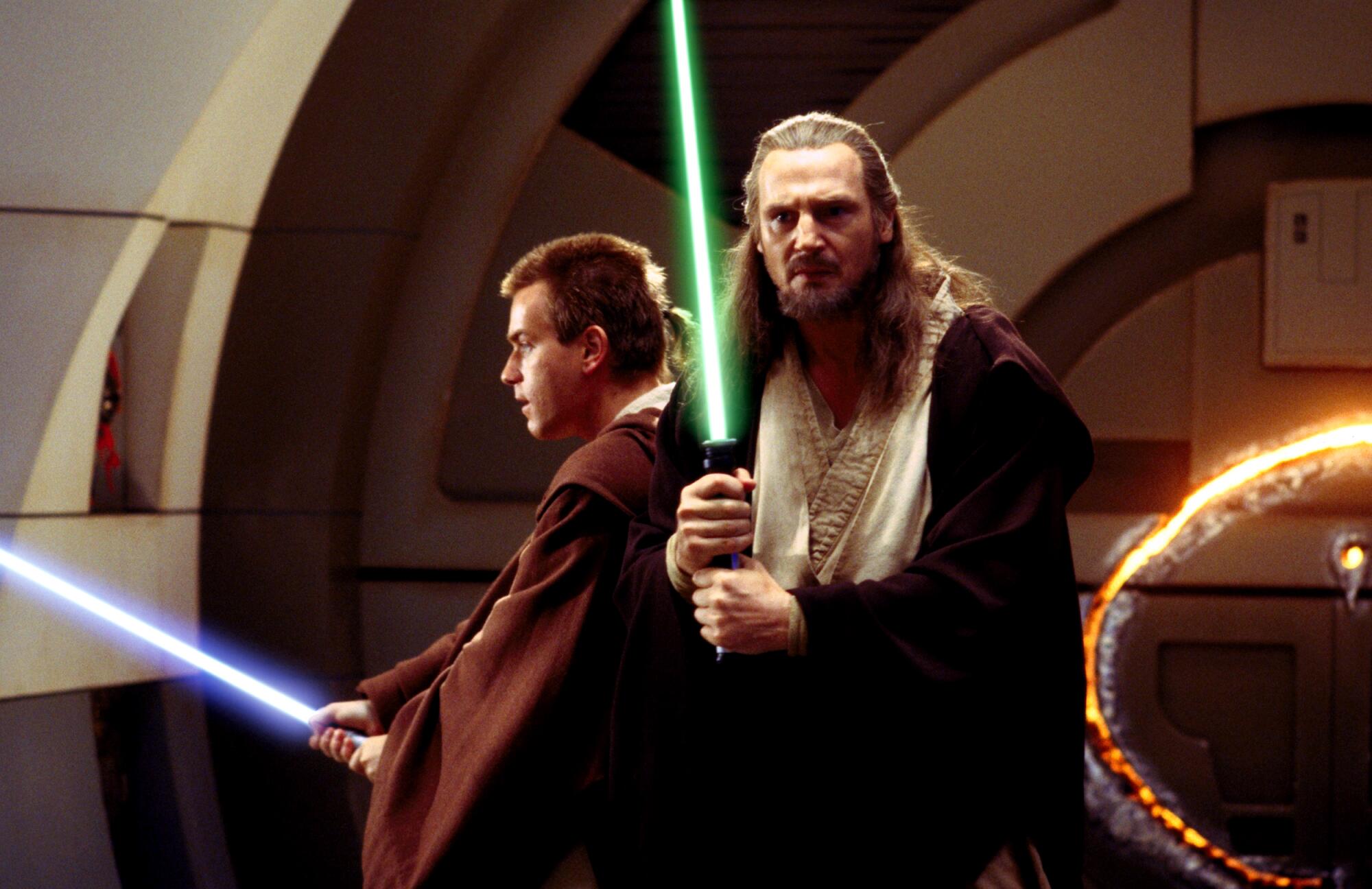 Two Jedi in robes wield lightsabres.