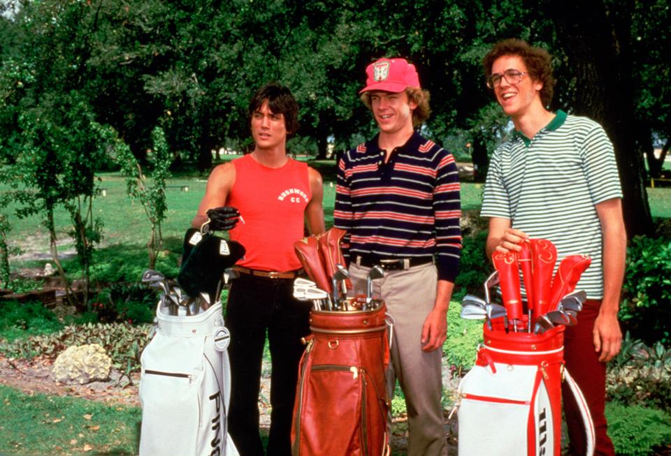 Three young men stand on a golf course, each carrying a golf bag.