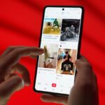A smartphone with fingers scrolling a social media app on a red background