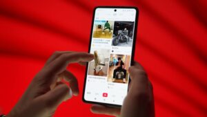 A smartphone with fingers scrolling a social media app on a red background