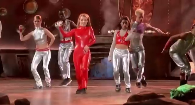 Britney Spears in a red bodysuit dancing with backup dancers in silver outfits.