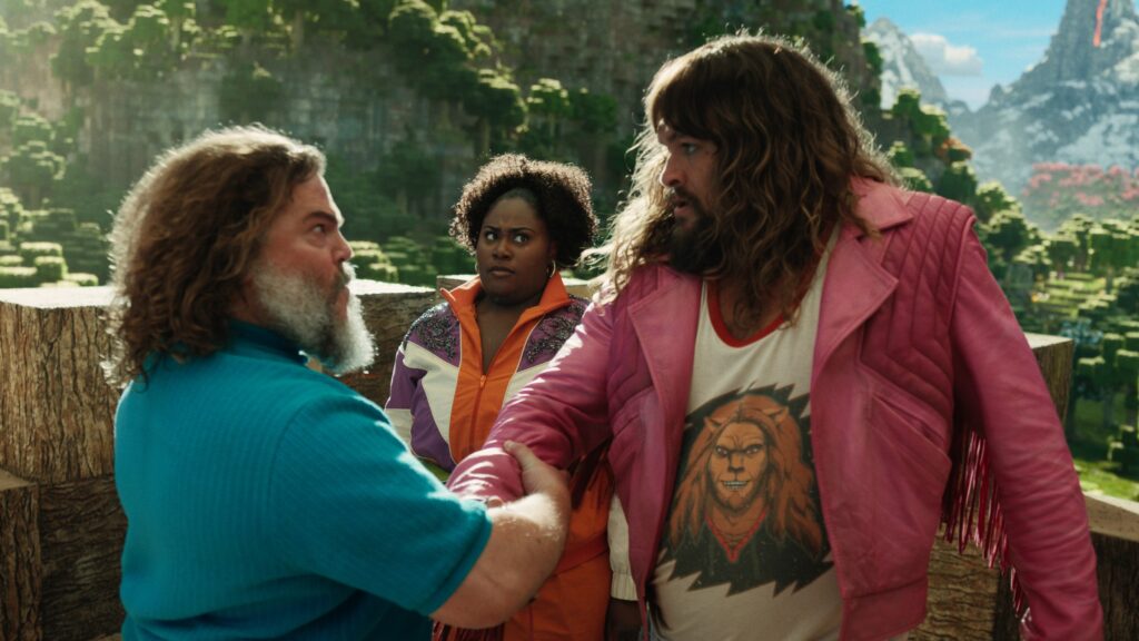 Steve (Jack Black) and Garrett (Jason Momoa) grip arms in an intense bro kinda way while Dawn (Danielle Brooks) looks on dubiously in A Minecraft Movie