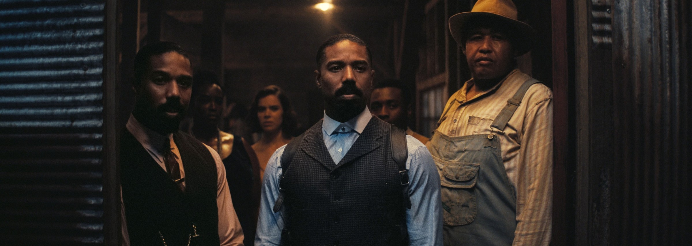 Black twins Smoke and Stack (both played by Michael B. Jordan) stand blocking the doorway to their juke joint alongside their bouncer Cornbread (Omar Benson Miller) in Ryan Coogler’s Sinners