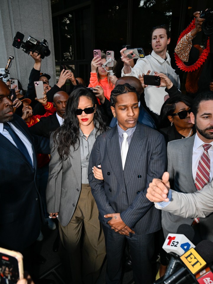 Rihanna and A$AP Rocky surrounded by photographers outside a courthouse.