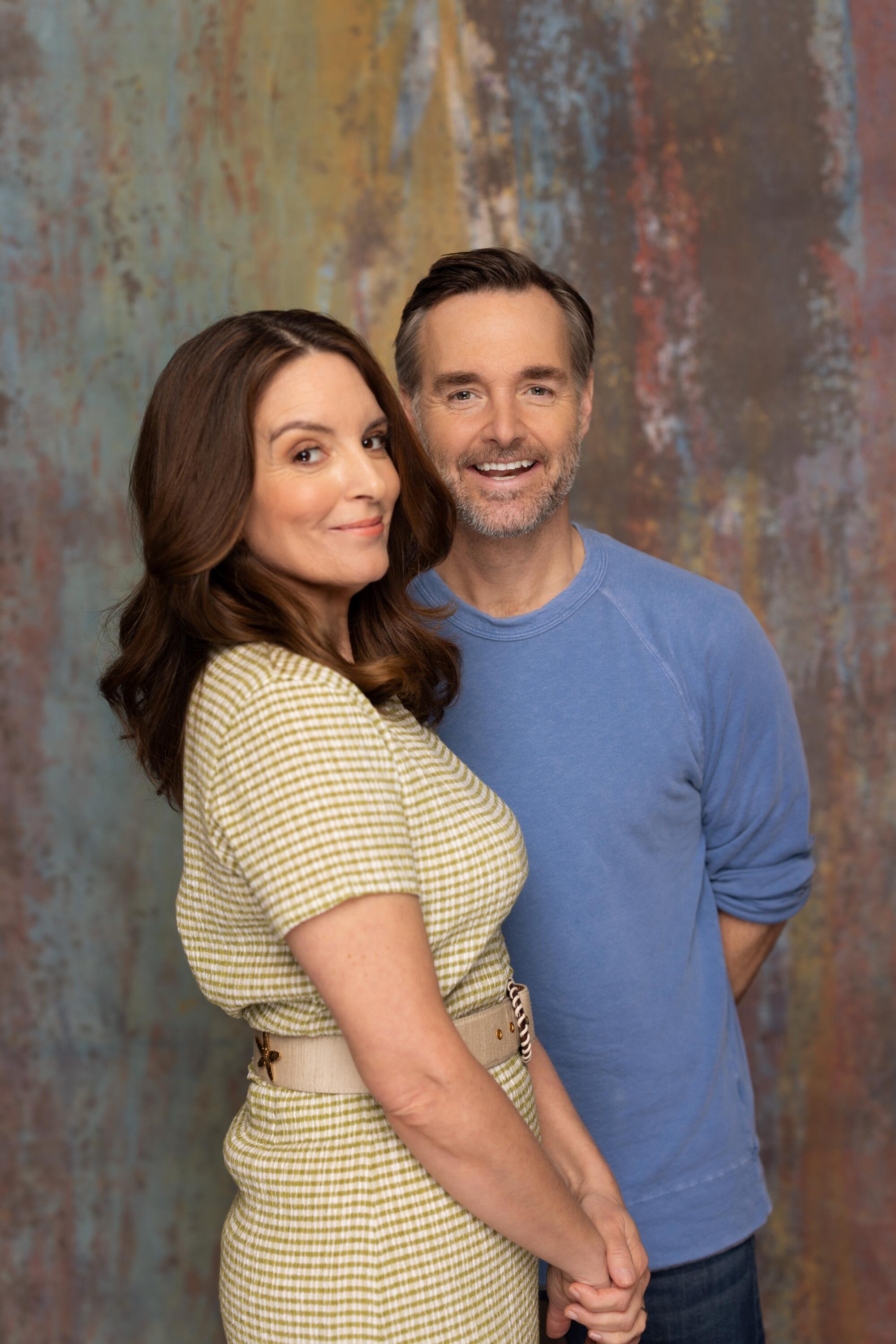 A woman in a dress with long brown hair stands in front of a man in a blue sweater.
